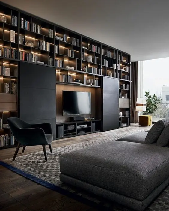 An elegant and refined black and grey living room with a huge lit up shelving unit on the wall and a TV hidden with sliding black panels.