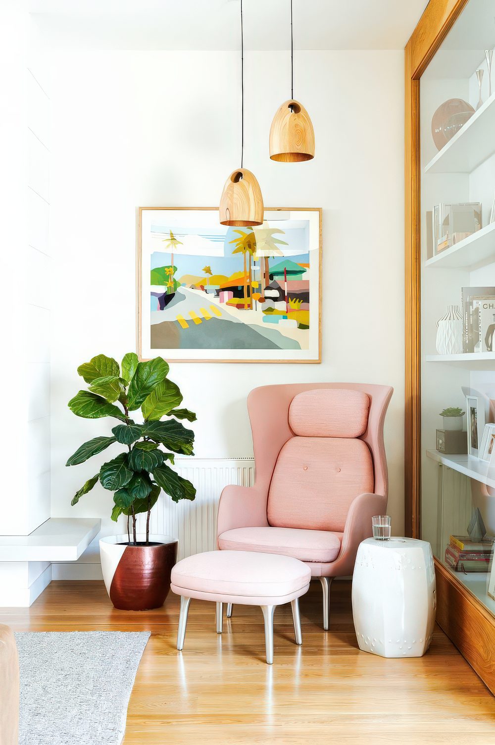 An awkward corner with a pink chair and a footrest, hanging wooden lamps and a side table for reading here.