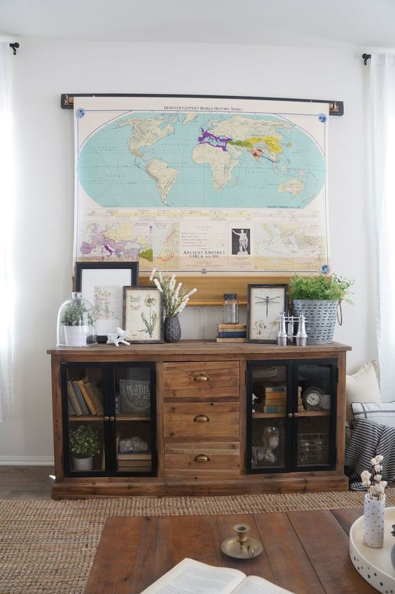 A stylish farmhouse space with a reclaimed wood storage unit, greenery, artwork and a large world map that hides the TV easily and effortlessly.
