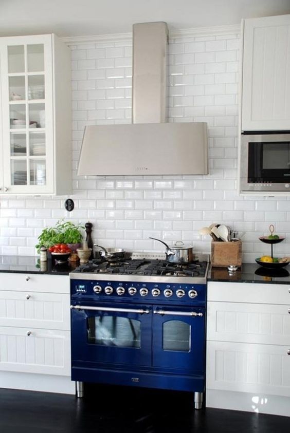 A traditional white kitchen is made eye-catchy with a subway tile backsplash and a cobalt blue cooker.