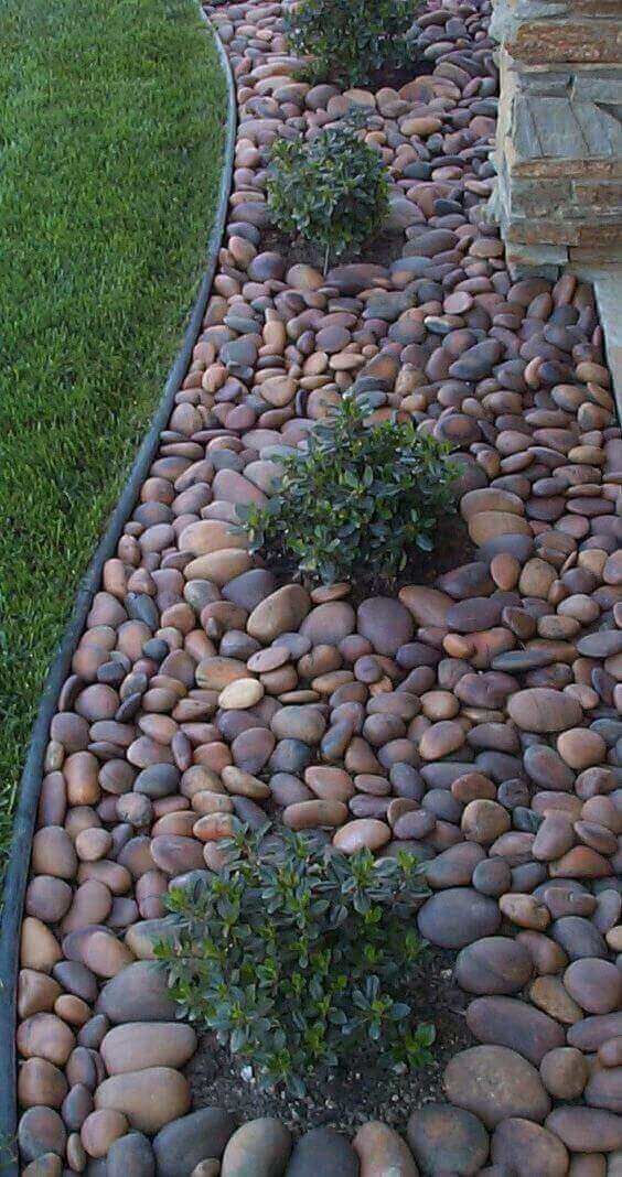 Chic and bold pebble garden edging with little greenery bushes growing inside it for a fresher and cooler look.