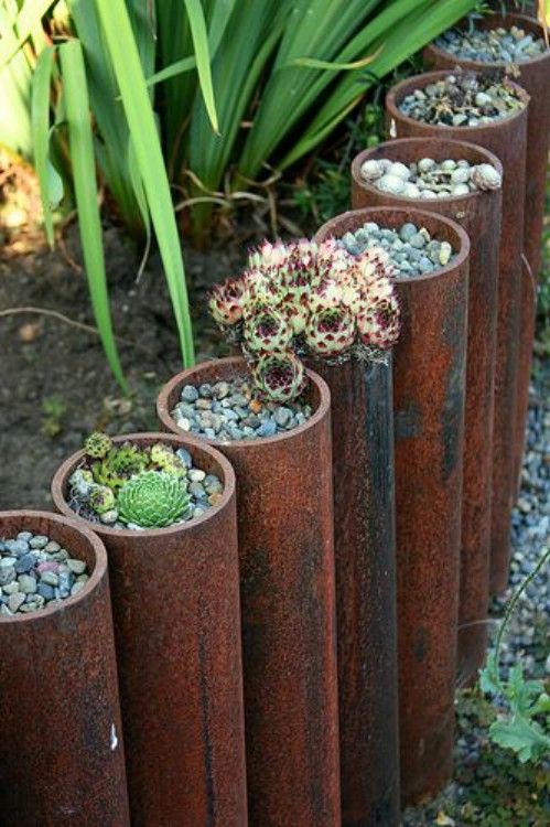 large metal pipes with succulents planted with pebbles in them is a unique and creative idea to border your garden.