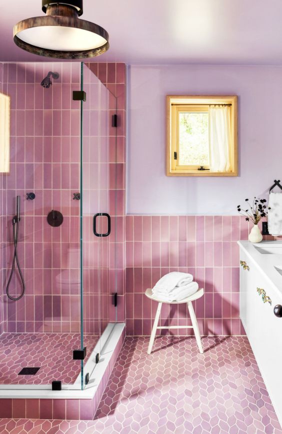 A bathroom with lilac walls and pink skinny and leaf-shaped tiles, a shower space, a white vanity and greenery is lovely.