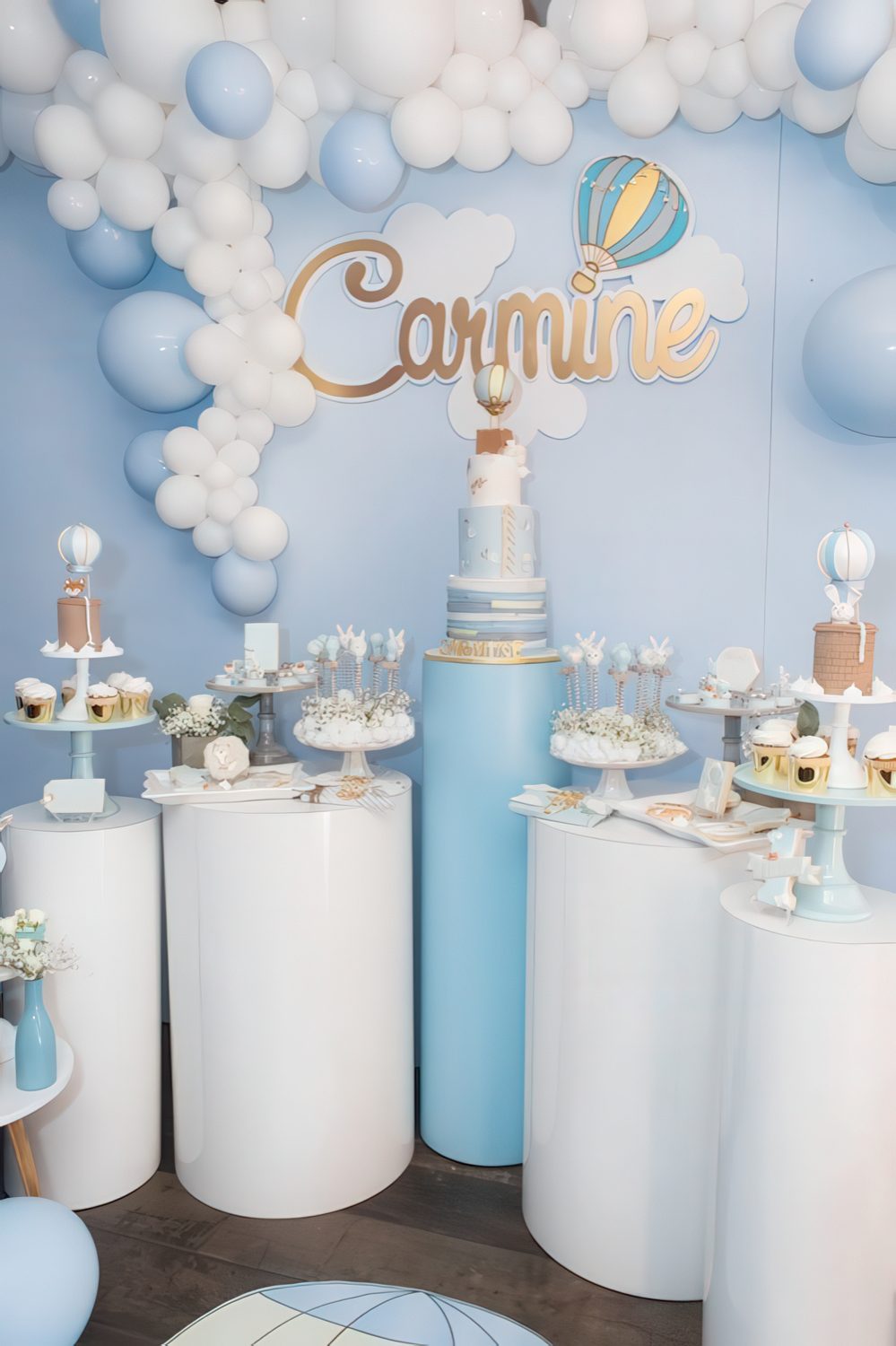 A blue and white pedestal dessert table with a hot air balloon backdrop, a balloon garland and lots of cute desserts.