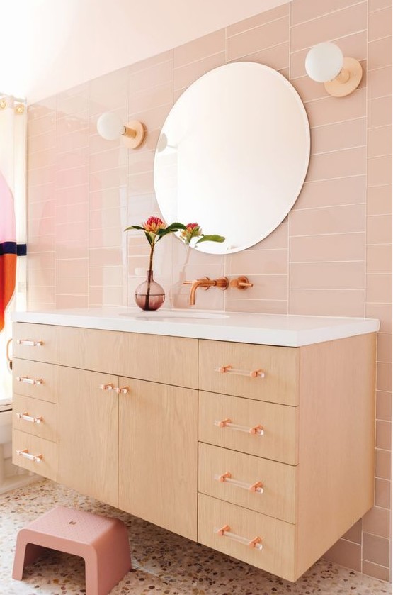 A chic blush bathroom designed with sleek skinny tiles, a stained floating vanity with clear glass handles, and a terrazzo floor. The pink stool adds a playful touch, making this bathroom both stylish and functional.