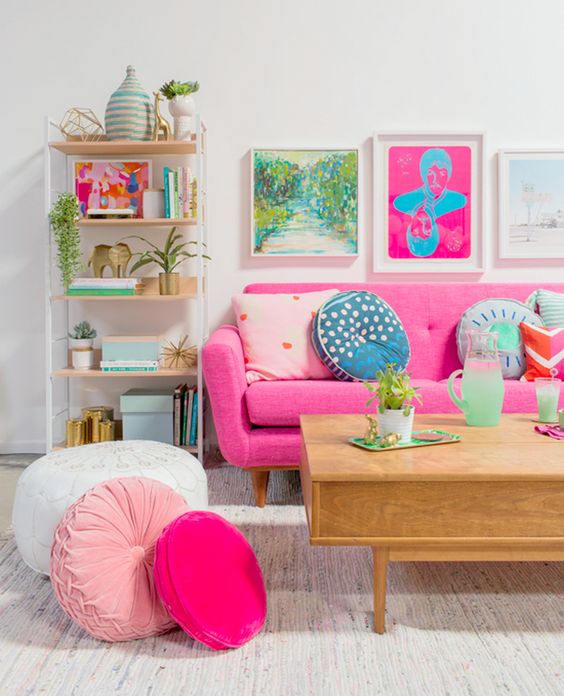 A bold living room with colorful artworks, a pink sofa and pink and blush pillows plus printed ones.