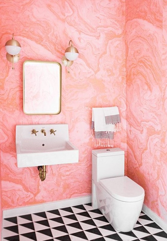 A bold powder room with pink watercolor wallpaper on the walls, black and white tiles and brass fixtures for more chic.