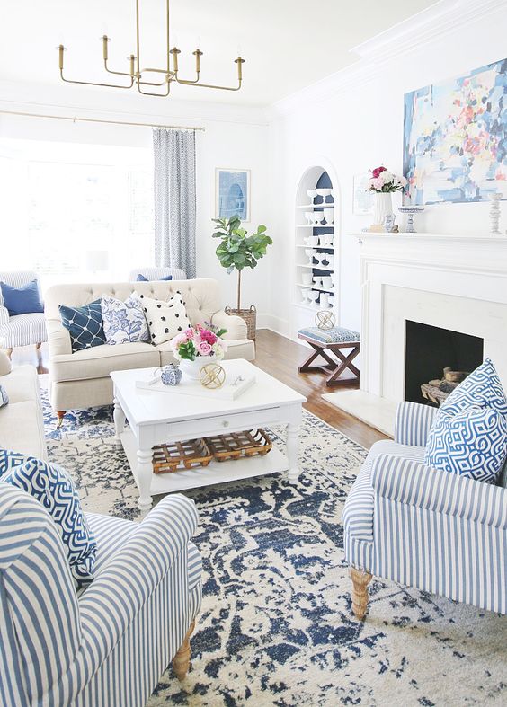 A bold summer living room with a printed rug, bold printed pillows and a striped chair plus greenery and blooms.
