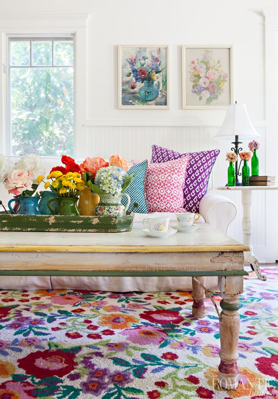 A bold summer living room with floral artworks, blooms in vases, printed pillows and a colorful floral rug for a cheerful feel.