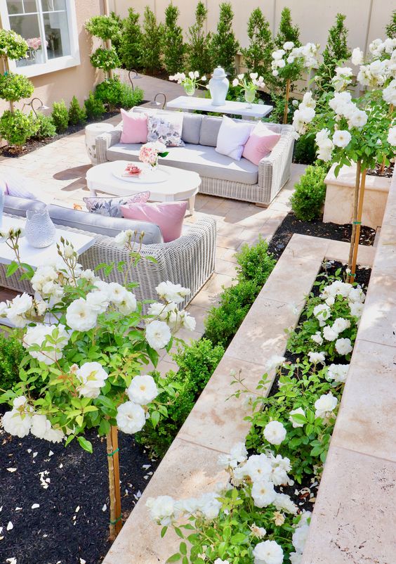A bright and vivacious summer terrace done with tiles, white wicker furniture, pastel upholstery and pillows and lots of greenery and blooms.