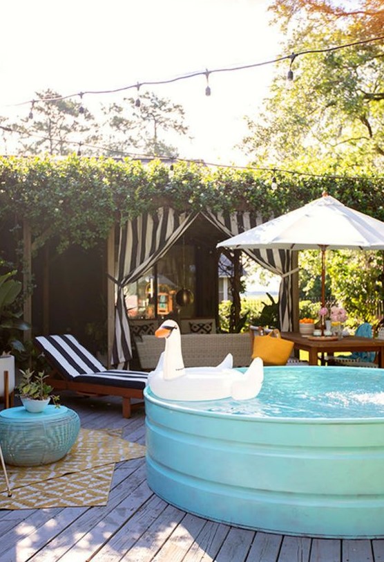 A bright patio with a sitting space, a dining space and a turquoise stock tank pool with a float, some loungers and layered rugs.