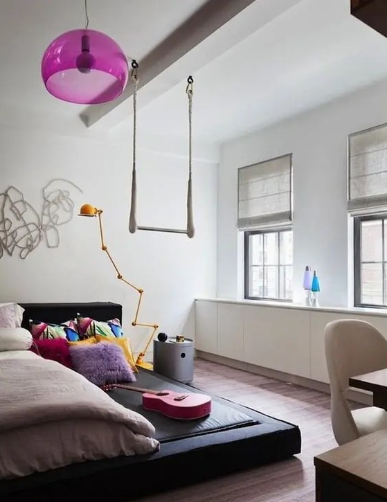 Discover a bright teen girl bedroom with a black platform bed and a hot pink pendant lamp. The colorful bedding adds vibrancy, while the simple shades maintain a clean look. This room is perfect for a cheerful and inviting space.