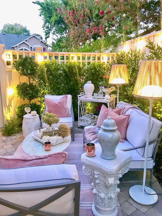 A chic pastel terrace with white contemporary furniture, floor lamps, refined tables and a greenery wall.