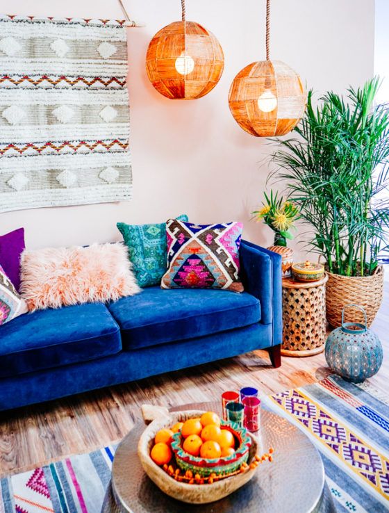 A colorful boho living room with a boho hanging, faceted lamps, a blue sofa, colorful pillows and a rug.