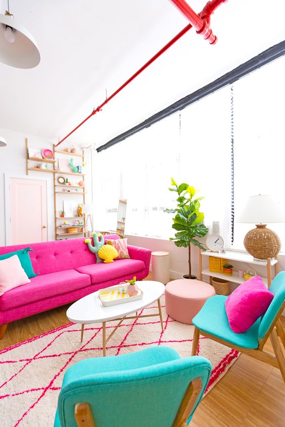 A colorful living room with a pink sofa, turquoise chairs, bright pillows of catchy shapes for fun.