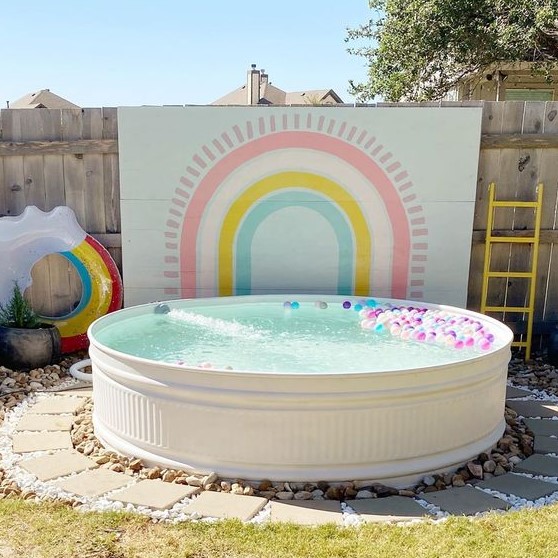 A colorful pool space with a lovely accent wall, a pool with colorful floats, a rainbow one is a lovely space for kids.