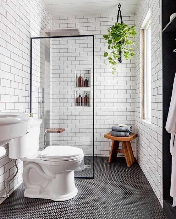 A contemporary bathroom includes penny and subway tiles. Built-in shelves, a sink, and a wooden stool enhance the functional space.