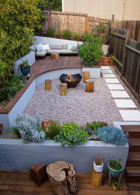 A contemporary terrace with a raised wooden deck, a gravel space with a fire pit and catchy plants.