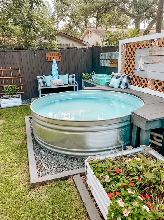 A cozy outdoor space with a stock tank pool, a grey bench, some more benches with pillows and potted plants.