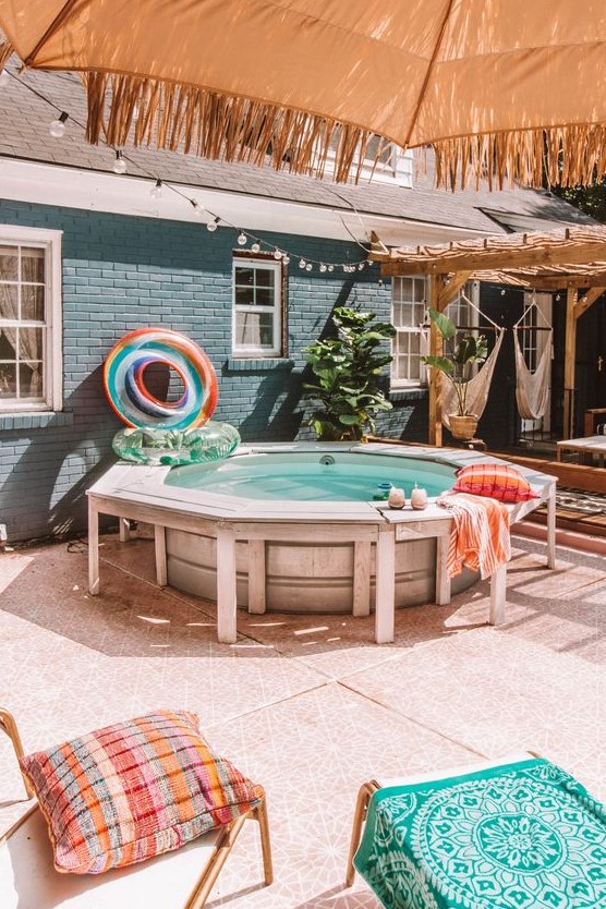 A funny and welcoming backyard pool space with a stock tank pool, a deck around, colorful floats and pillows and cushions around.