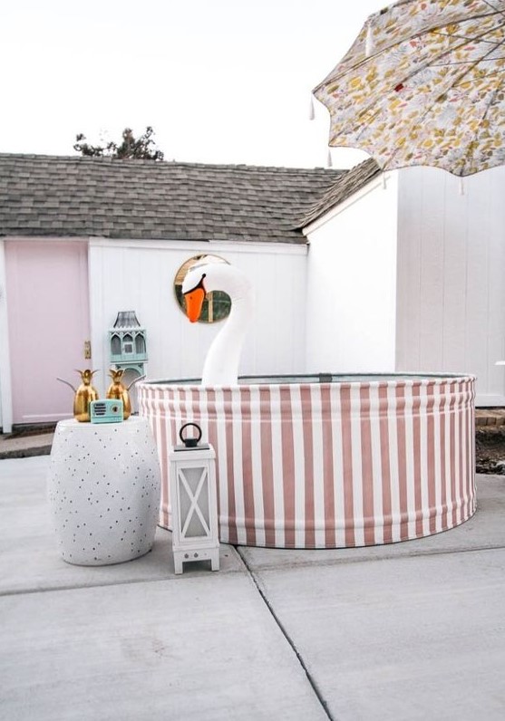 A funny backyard pool space with a striped stock tank pool, a side table with pineapple decor, candle lanterns and a float.