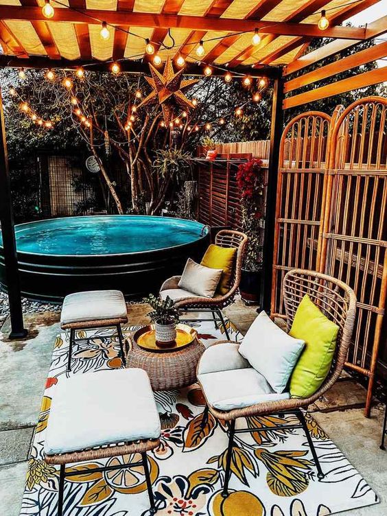 A gorgeous backyard with a black stock tank pool, a bright rug, rattan chairs and stools and a rattan coffee table.