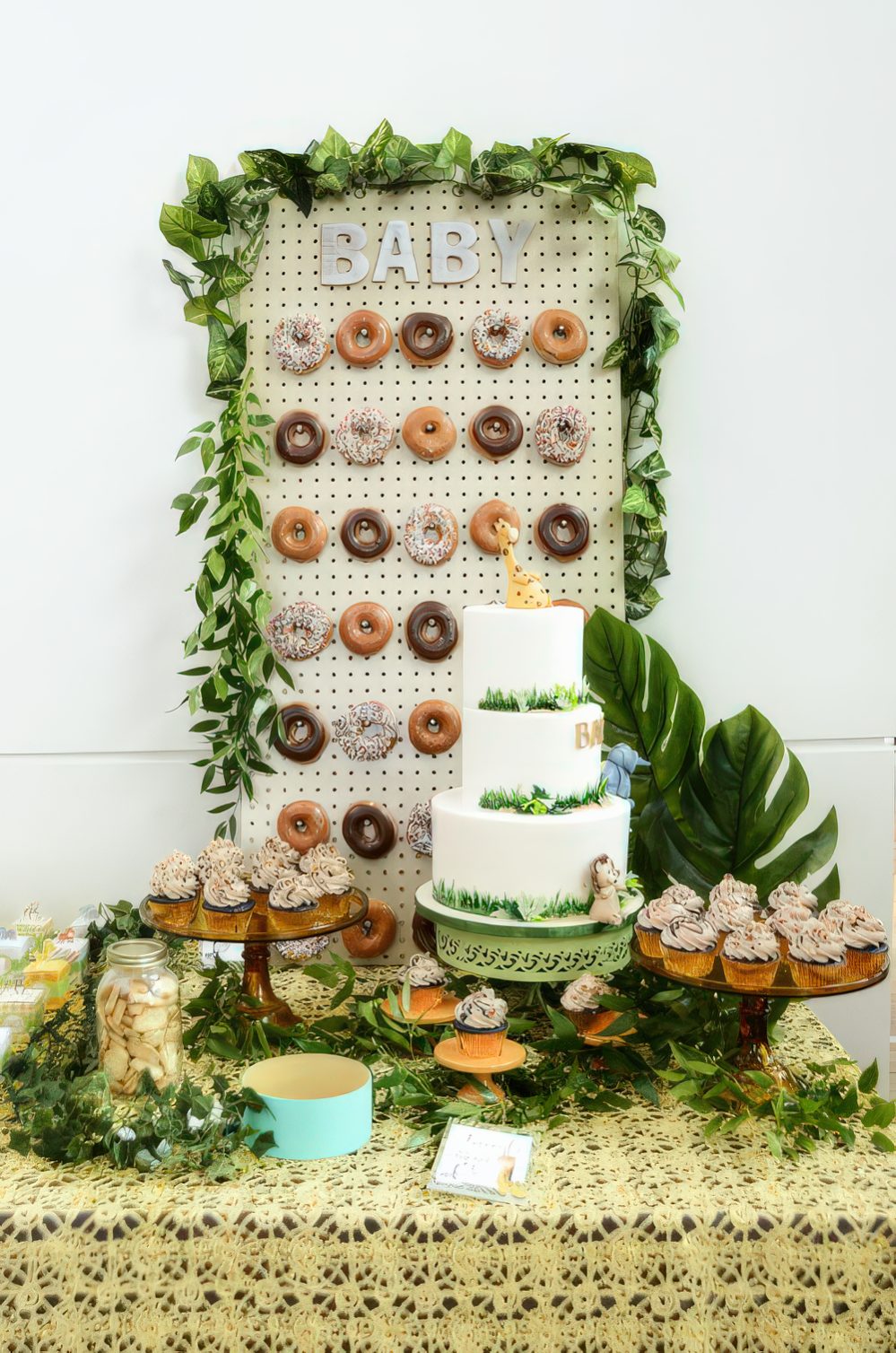A jungle-themed dessert table with a donut wall, tropical leaves, lots of greenery and a large cake is a chic idea.