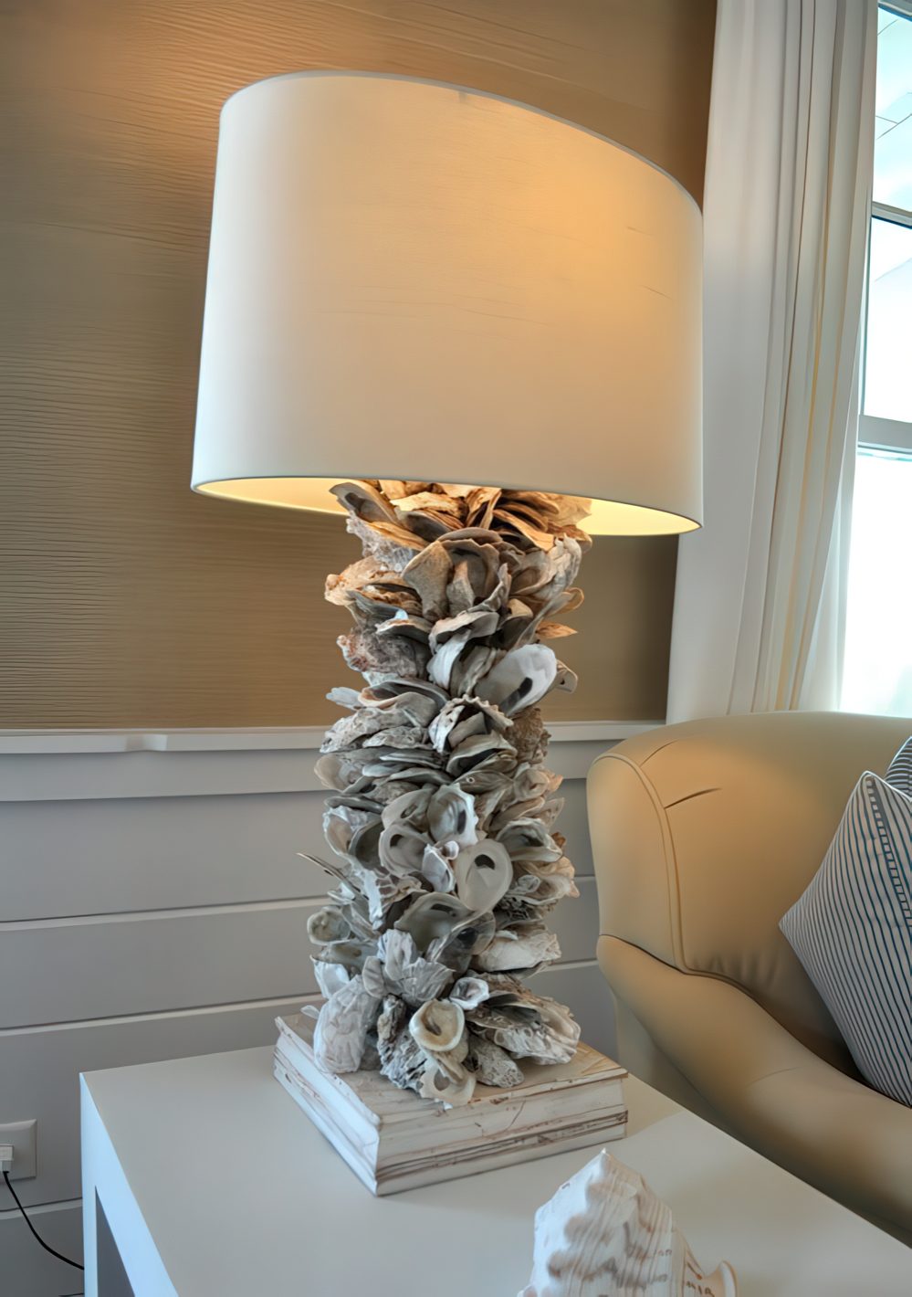 A large lamp with a neutral shade and lots of seashells covering the base looks very coastal and seaside.