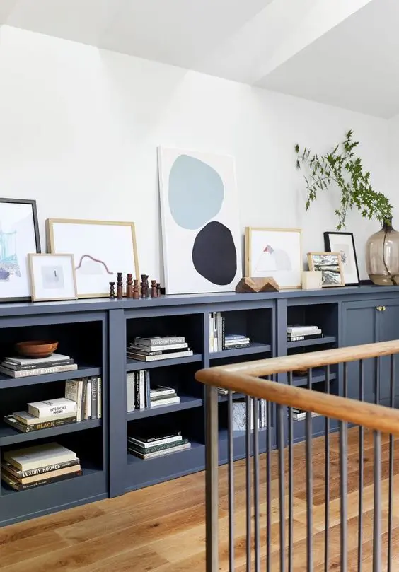 A large navy sideboard with open and closed storage compartments, with books, decor, artwork and greenery is amazing.