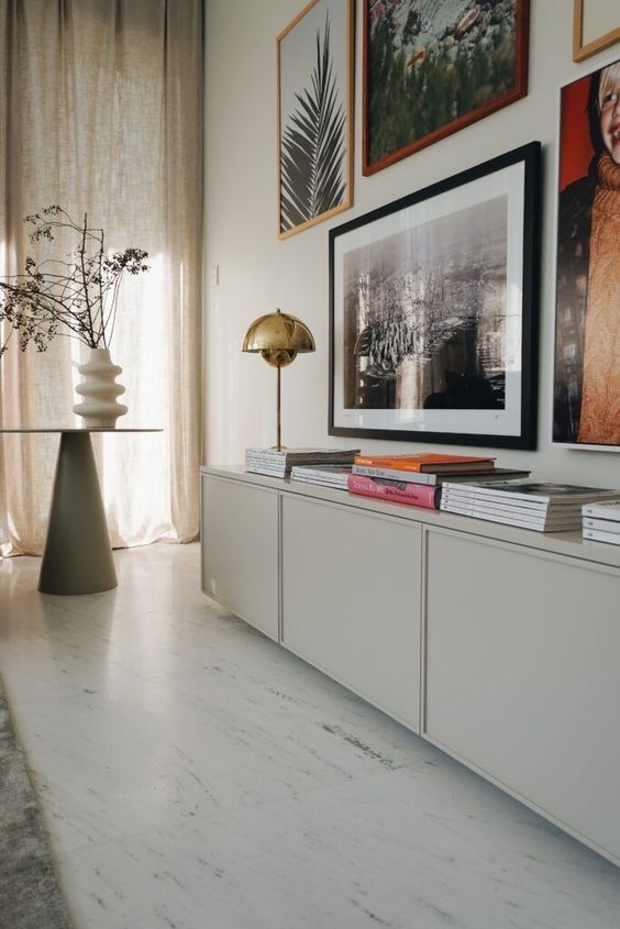 A light grey sideboard of IKEA Metod units, with books and a gold table lamp plus a gallery wall.