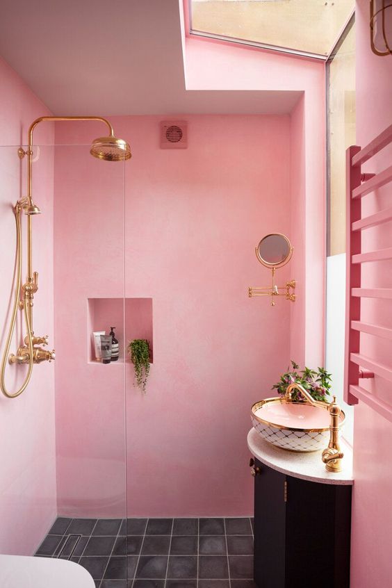 A light pink bathroom with a shower space, a niche shelf, a black vanity with a bowl sink and gold fixtures.