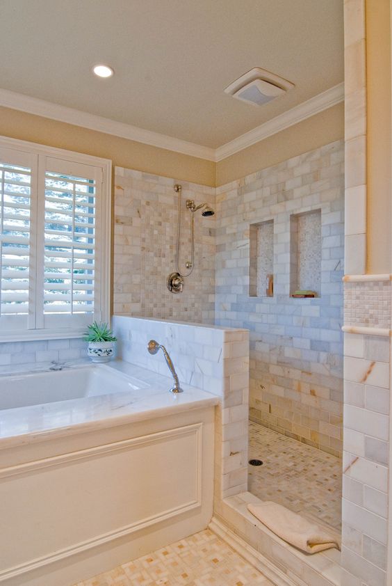 A lovely bathroom clad with marble tiles, with a half wall in the shower space, a bathtub clad with panels.
