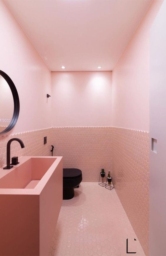 A lovely blush powder room with light pink walls and hex tiles, a pink vanity with a bilt-in sink and black fixtures for a contrast.