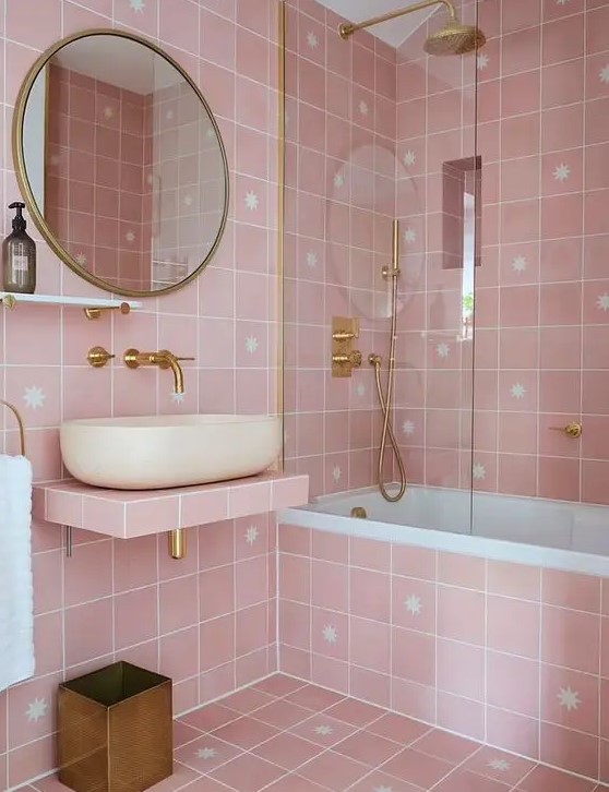 A lovely pink bathroom with pink star tiles, a floating vanity, a tub, gold fixtures and details.