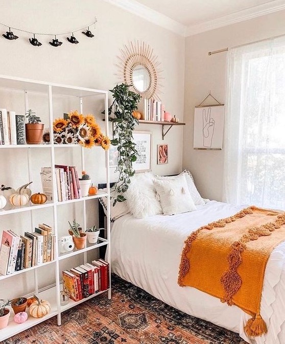 Design a lovely teen room with a black bed and a large open storage shelf decorated with blooms and pumpkins. A shelf and a mirror over the bed enhance the look. This room combines practicality with a charming aesthetic.