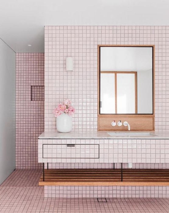 A millenial pink bathroom with a floating vanity clad with tiles, stained wood and black grout to make a contrast.