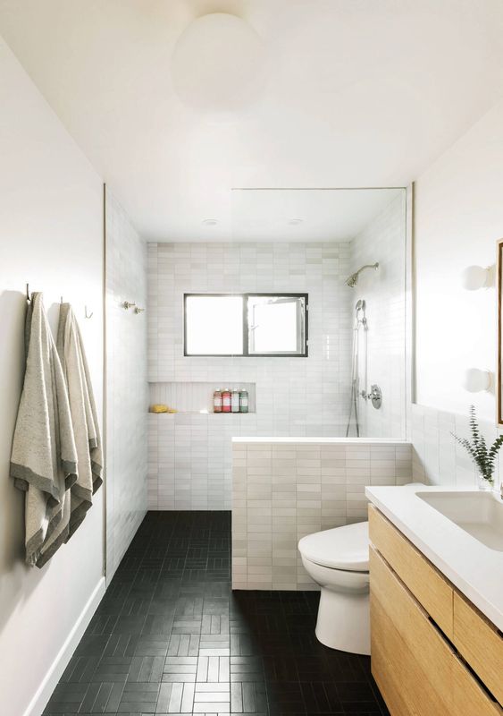 A modern bathroom with marble skinny tiles and black ones on the floor, a floating wooden vanity, a built-in niche for storage.
