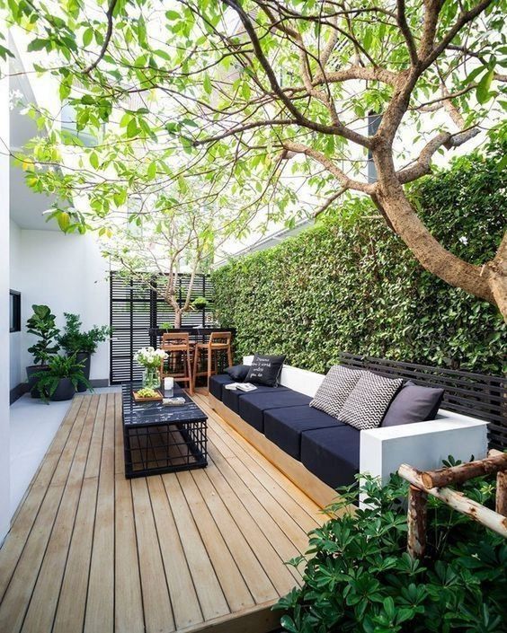 A modern monochromatic terrace with a wooden deck, a large built-in sofa, a small bar space and a whole living wall.