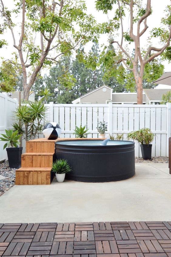 A modern outdoor space with a black stock tank pool, a wooden deck, potted plants and lights - who needs more.