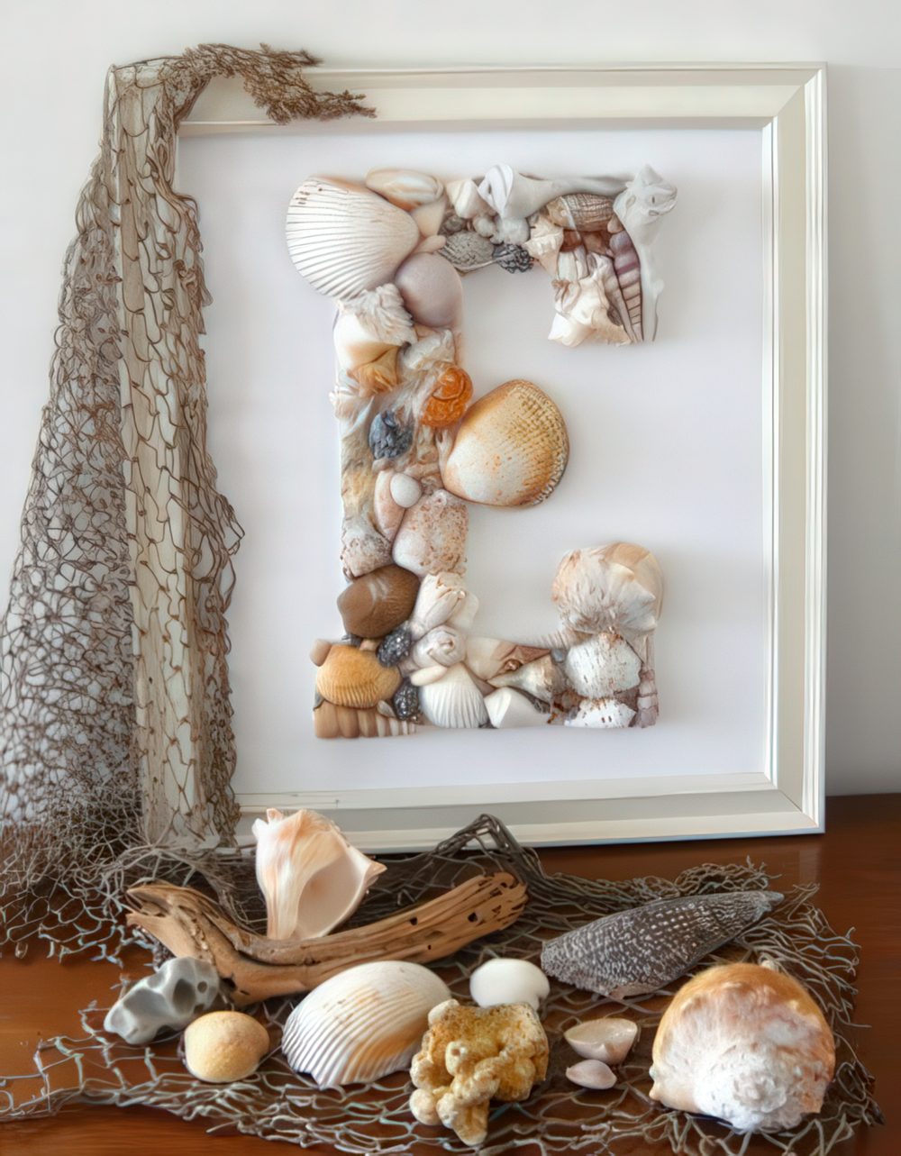 A monogram seashell artwork and some corals and seashells on fishing net for coastal and beachy decor.