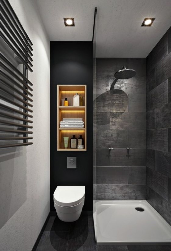 A moody black bathroom with stone-inspired tiles, a wall shelf with lights, a shower space.