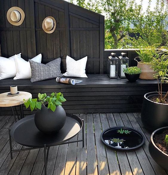 A moody terrace with black wood, light pillows, potted greenery and candle lanterns looks fresh and stylish.