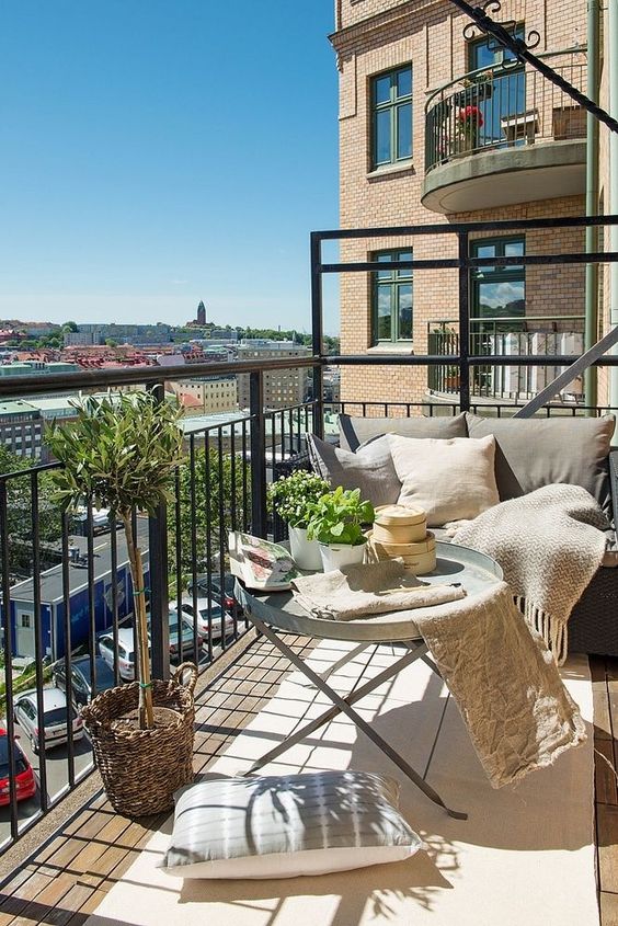 A neutral balcony with metal furniture, neutral textiles, potted greenery and lots of pillows is very welcoming.