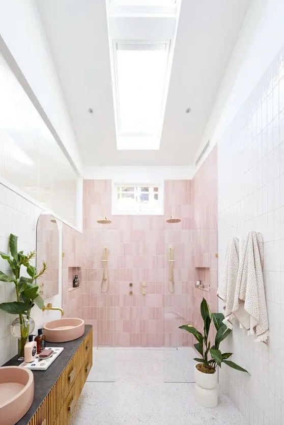 A floating vanity and pink sinks bring modern elegance to this neutral bathroom with a skylight and pink accent wall. Potted plants add a touch of nature. Opt for floating fixtures and colorful accents for a chic bathroom design.