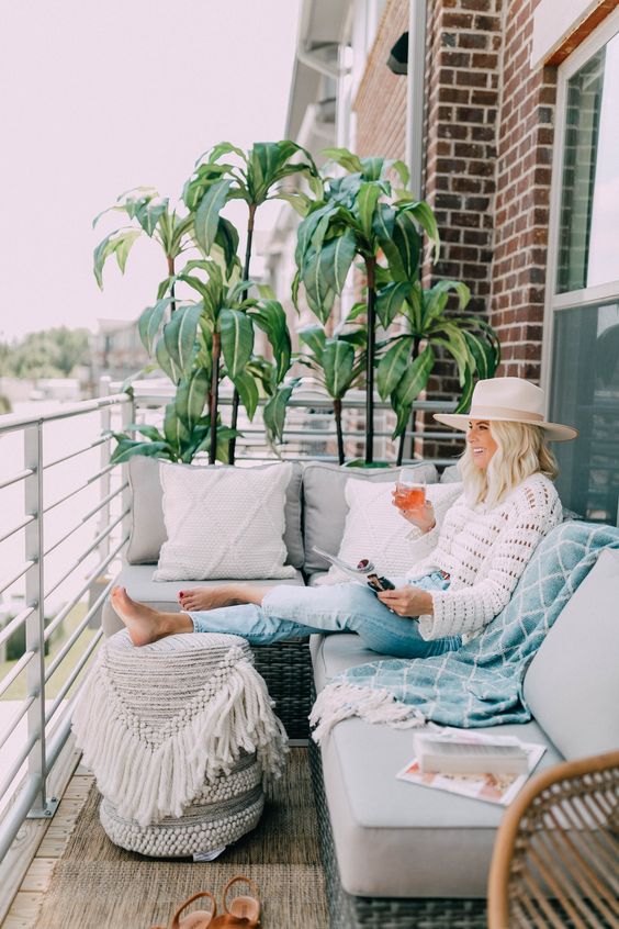 A neutral boho balcony with wicker furniture, neutral upholstery, potted greenery and boho textiles for more coziness.