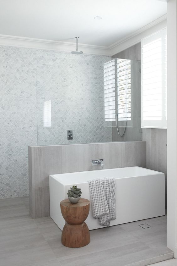 A neutral contemporary bathroom with marble fish scale tiles and a half wall covered with neutral wood plus the same on the floor.