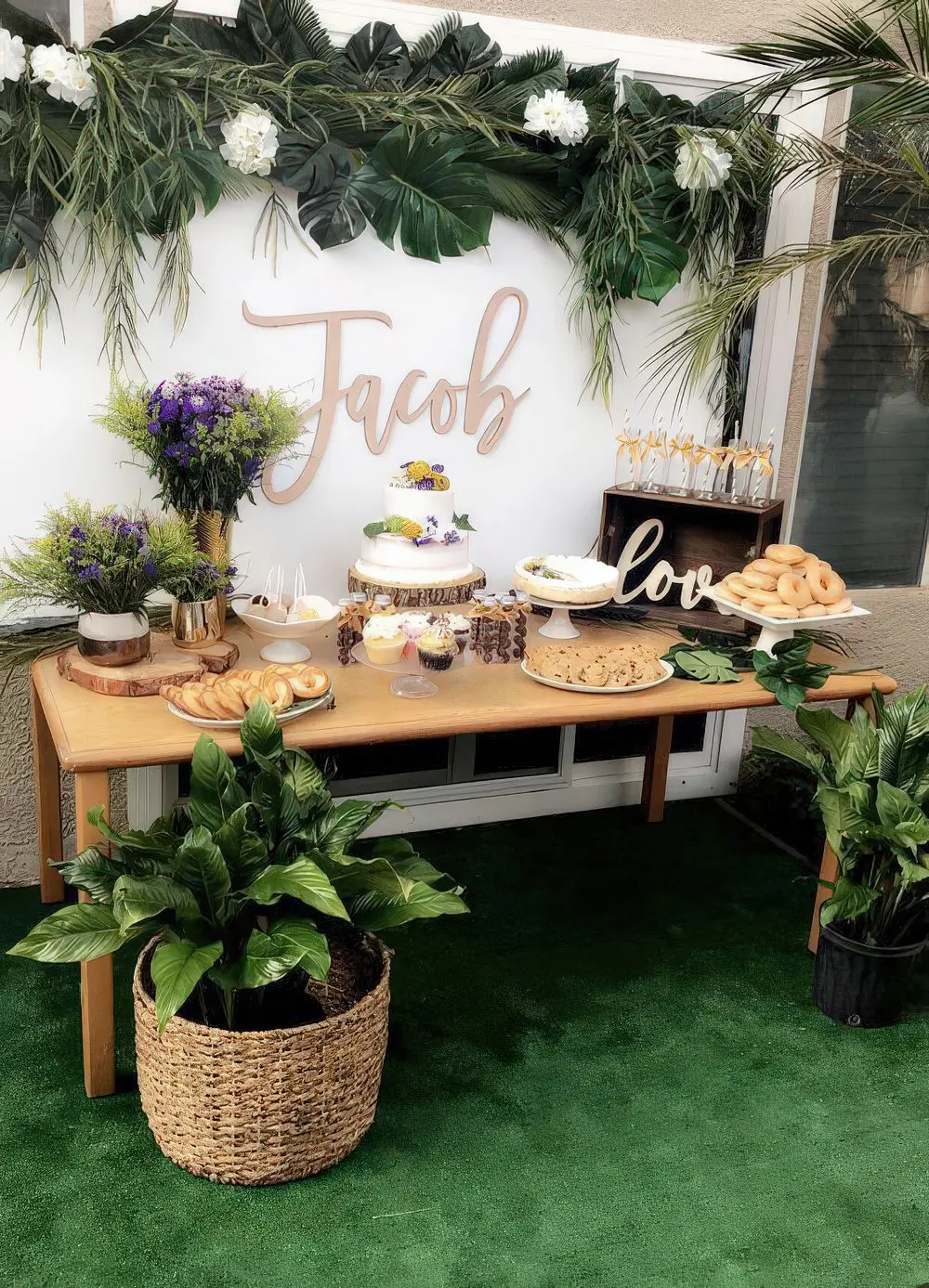 A neutral dessert table with tropical leaves and plants, with white and purple blooms and lots of sweets.