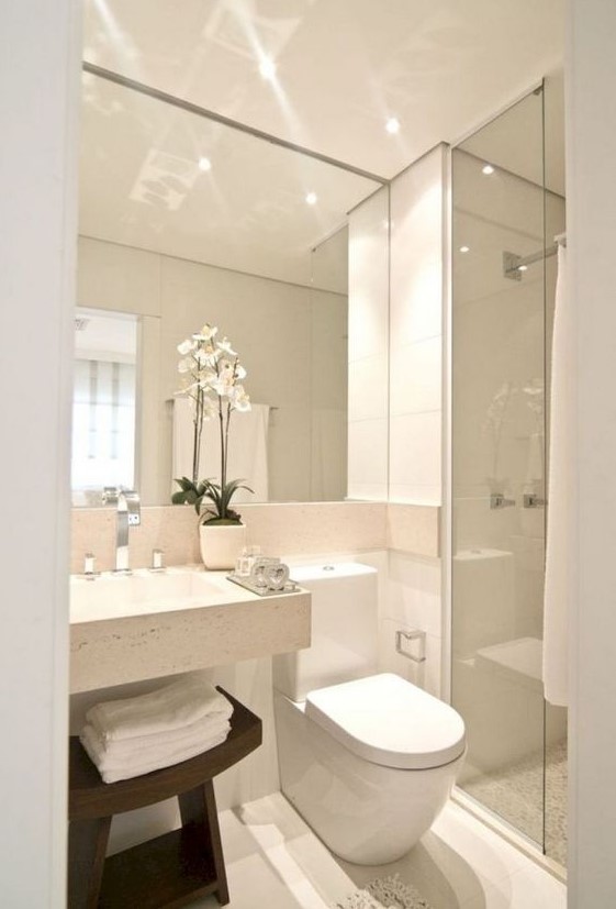 A neutral minimalist bathroom with a large mirror, a square sink, a shower space and a dark stained wooden stool.