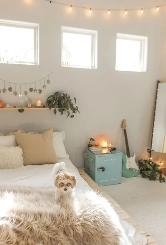 Create a neutral teen bedroom with neutral walls, a pallet bed, and a floor mirror. A blue storage cabinet and a floating shelf with greenery and candles bring life to the room, while a guitar adds a musical vibe. This design combines simplicity with style.