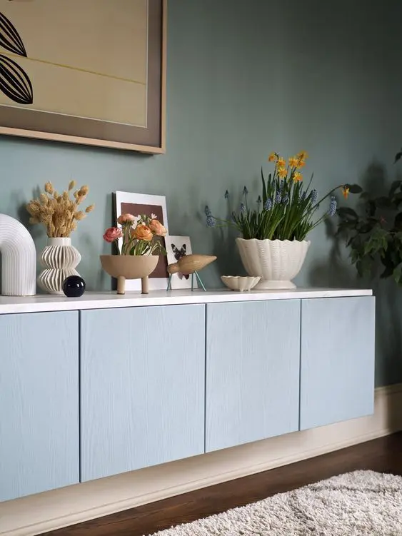 A pastel blue floating credenza of IKEA Metod units, white countertop, blooms, plants and chic decor.